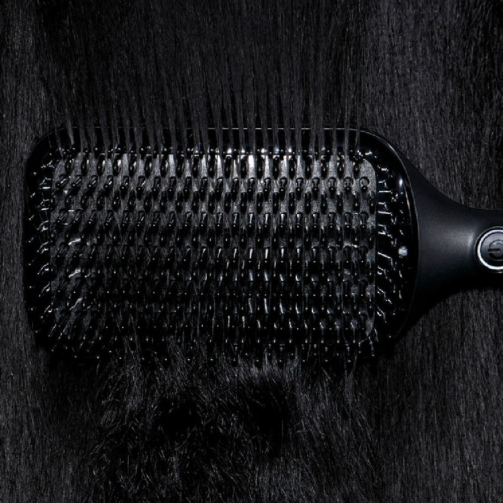 Black paddle hairbrush on a dark textured surface
