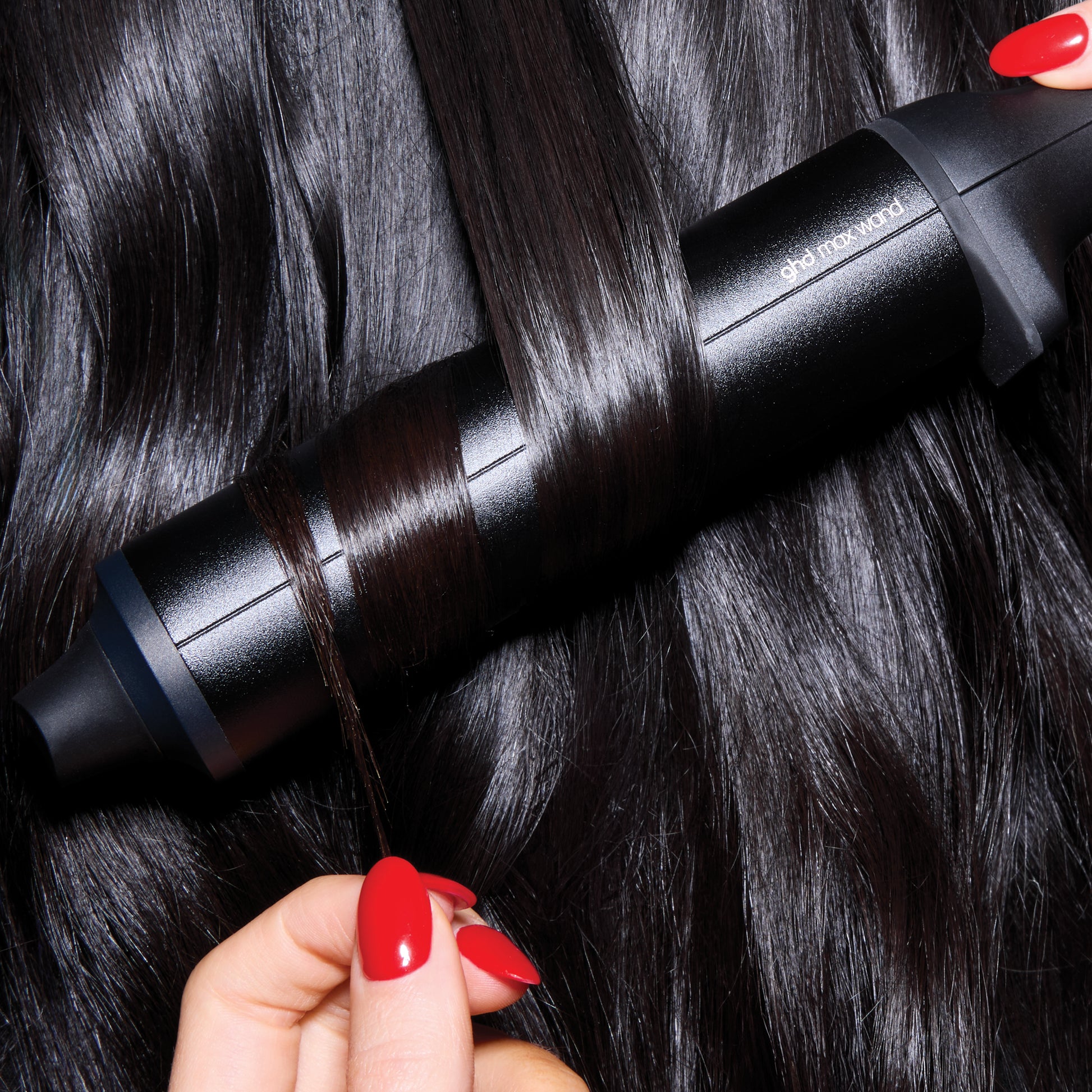 Person using a black hair straightening device on dark hair with red nail polish.